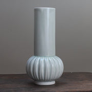Tall pale green vase with a straight top and curved bottom on wooden table