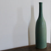 a green glazed ceramic bottle on a wooden table it's by ceramicist Lucy Burley.