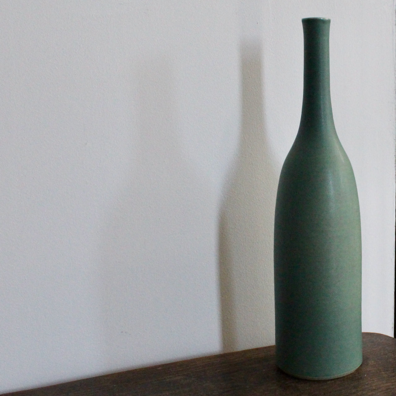 a green glazed ceramic bottle on a wooden table it's by ceramicist Lucy Burley.