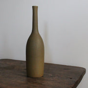 an olive coloured ceramic bottle on a wooden table it's by UK ceramic artist Lucy Burley