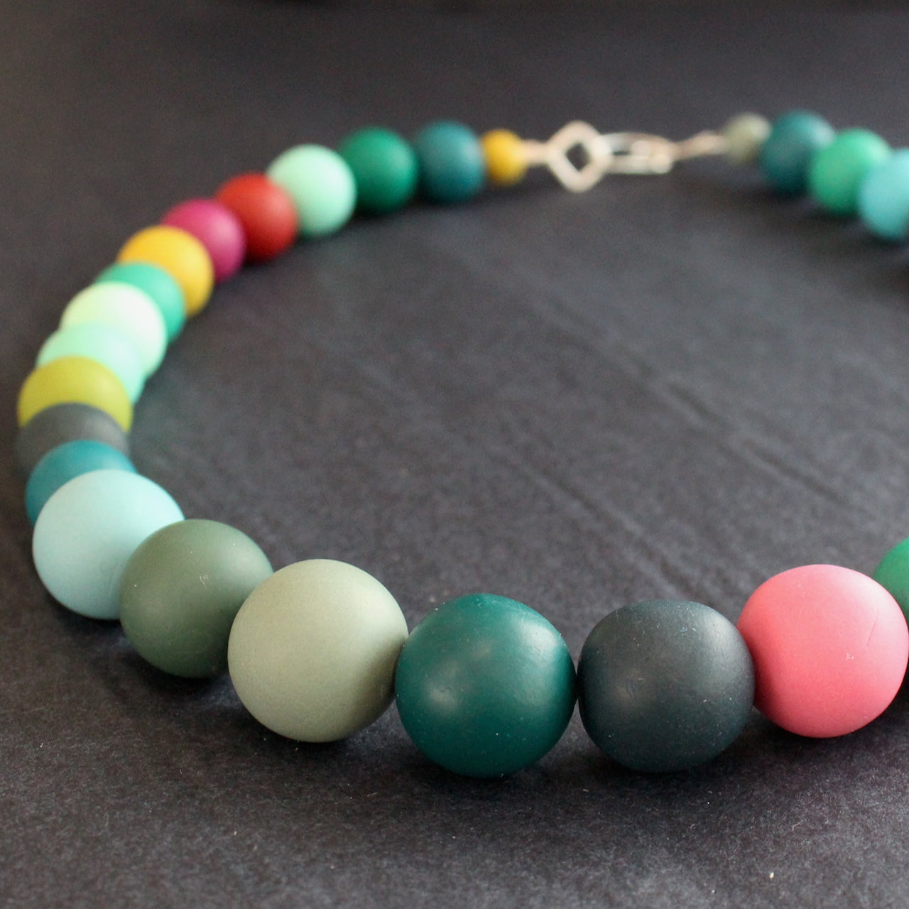 close up detail of a Claire Lloyd necklace of round beads in greens, pinks, blues and yellow