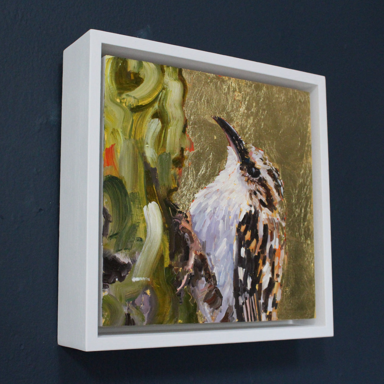 a framed Jill Hudson painting of a tree creeper bird with white plumage, brown beak on a gold background