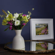 A vase of flowers next to a Jill Hudson framed abstract landscape painting