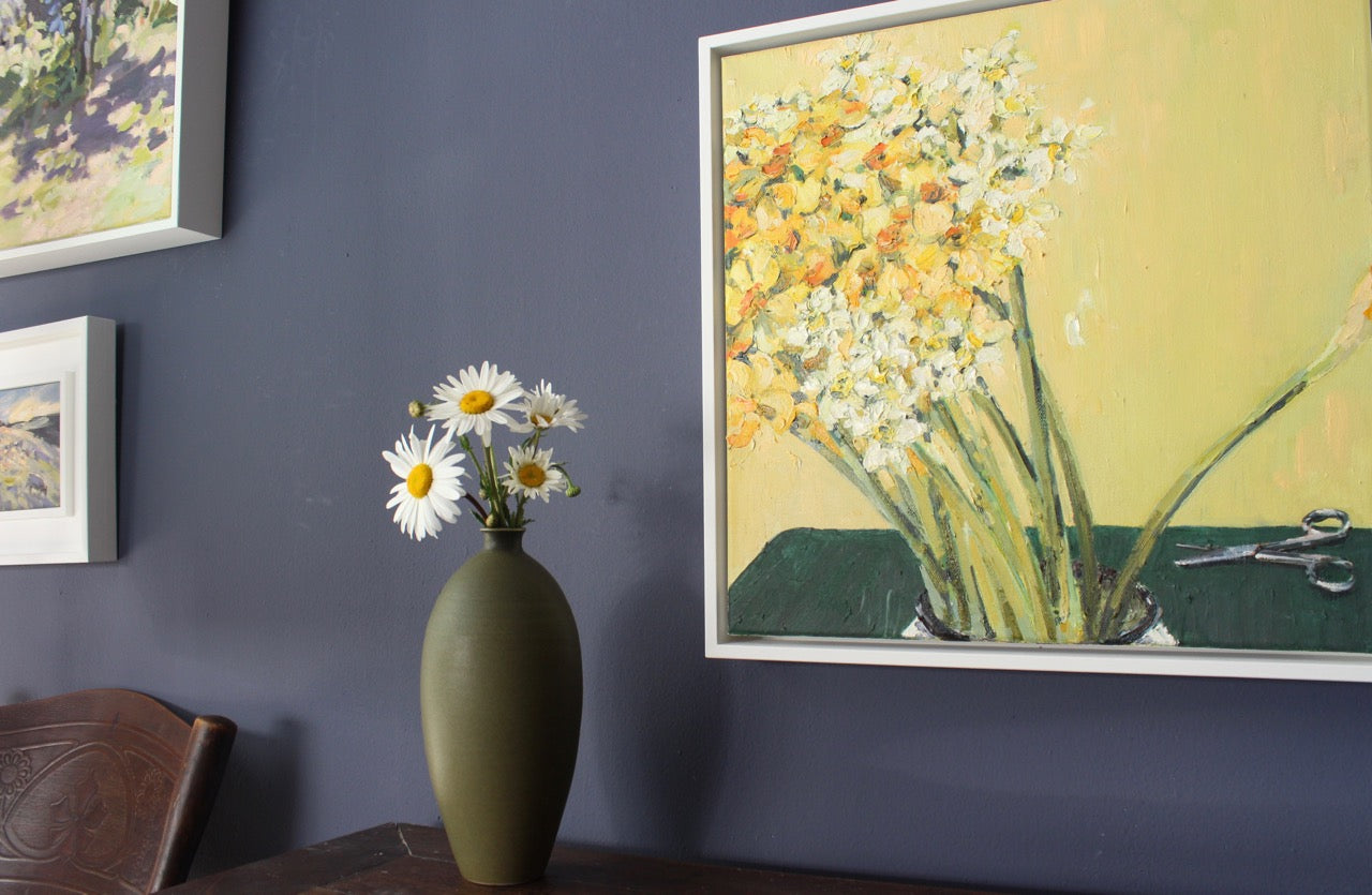 Dark green bottle with daisies in it next to painting of daffodils