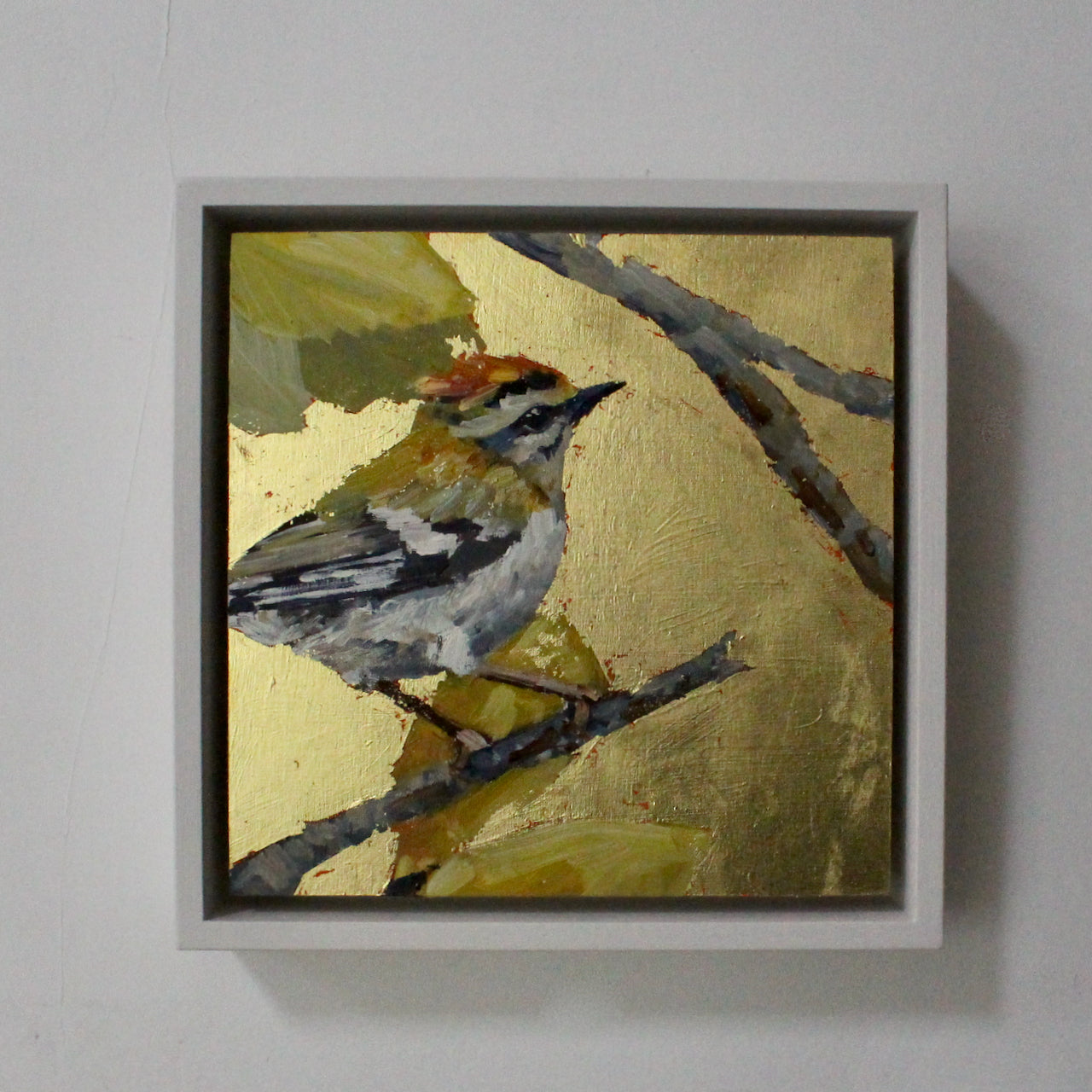 a framed Jill Hudson painting of Fire Crest bird on a tree with a gold leaf background.