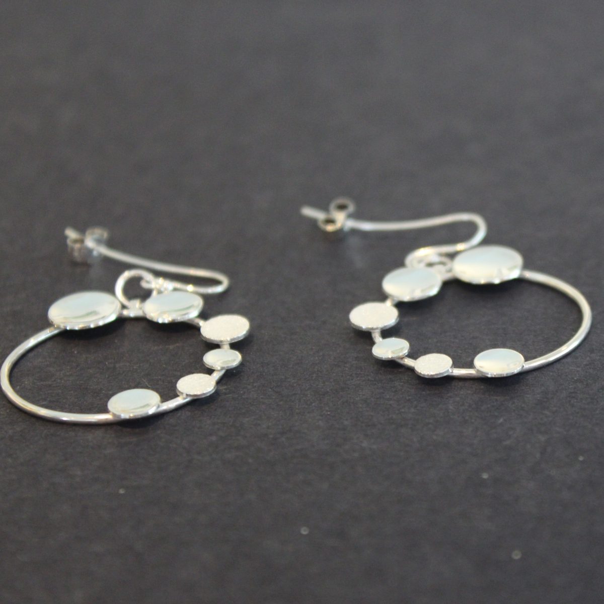 A pair of Round silver hoop earrings with small silver circles attached by Beverly Bartlett