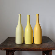 A trio of Lucy Burley ceramic bottles in shades of yellow on a wooden table.