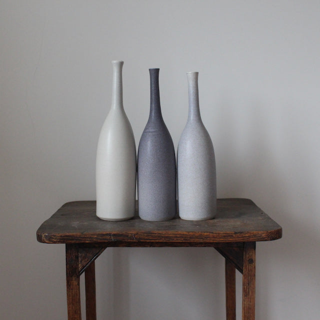 Trio of ceramic bottles in shades of grey on a wooden table by Lucy Burley