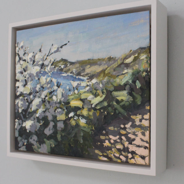 A framed painting on a wall by Jill Hudson called April Blossomof white blossom on coastal path in Cornwall.