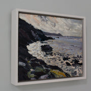 A framed painting of Rame Head in Cornwall by Jill Hudson, called From the Rocks  showing grey sea with dark cliffs