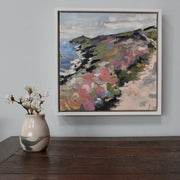small vase with white blossom in it on a wooden table next to a painting of Rame Head in Cornwall by Jill Hudson