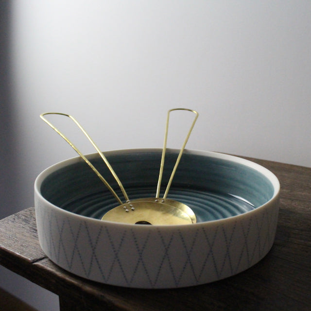a white porcelain serving dish with blue interior and blue diamond pattern on outside and brass sand servers in it, it's by Kathryn Sherriff of By the Line Pottery