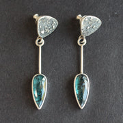 Long sliver earrings with a textured silver triangle falling to green oval shaped stones set in plain silver