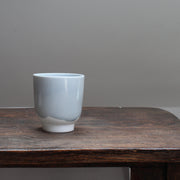 Small kiln shaped pale bluSmall pale ceramic beaker  with a white bottom on a wooden table