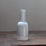 Small kiln shaped pale blue bottle with a white bottom on a wooden table