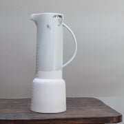 Tall pale green vase with grey pattern of flowers standing on a wooden table