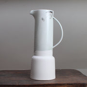 Tall pale green vase with grey pattern of flowers standing on a wooden table