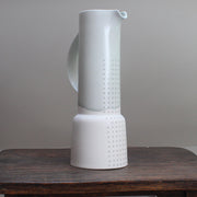 Tall pale green vase with a partial pattern of small grey dots standing on a wooden table