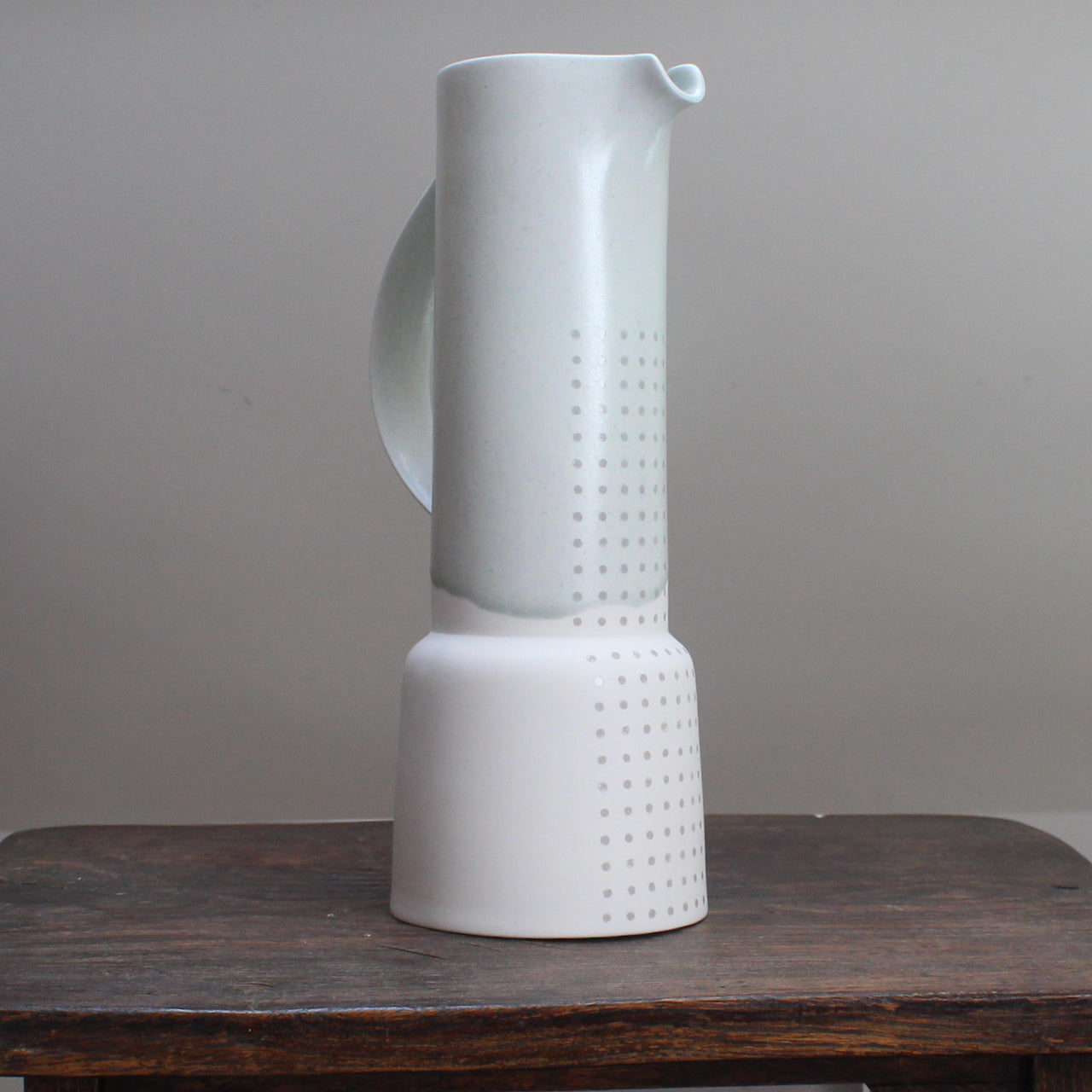 Tall pale green vase with a partial pattern of small grey dots standing on a wooden table