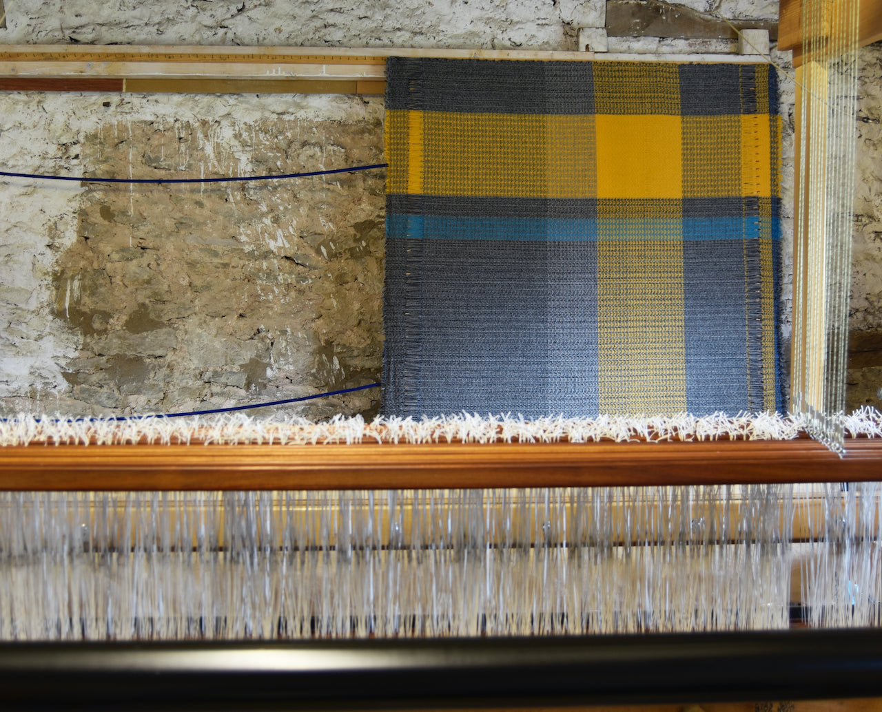 a Rhian Wyman woollen throw in grey, ochre and blue on a loom.