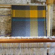 a Rhian Wyman Design woollen blanket in grey, ochre and blue on a loom