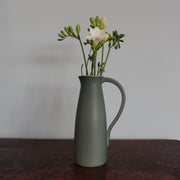 Olive green ceramic jug with handle with flowers in it by Lucy Burley on wooden table at the Byre Gallery