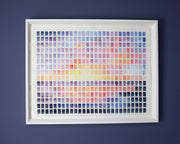 Abstract painting of a sunset pink, yellow and blue. Framed on dark blue wall.