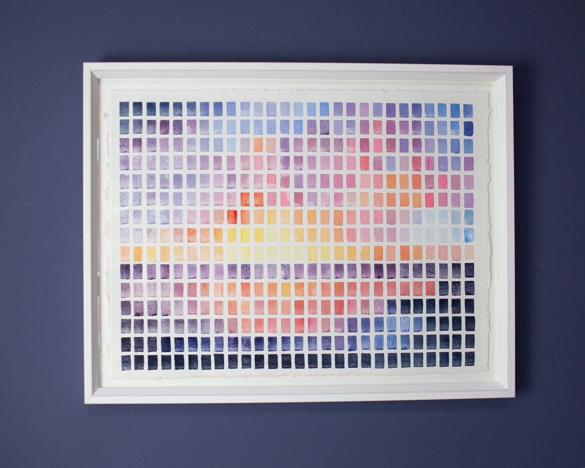 Abstract painting of a sunset pink, yellow and blue. Framed on dark blue wall.