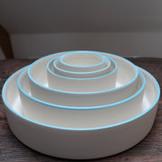 Six stacked white round bowls with a blue rim on a wooden table