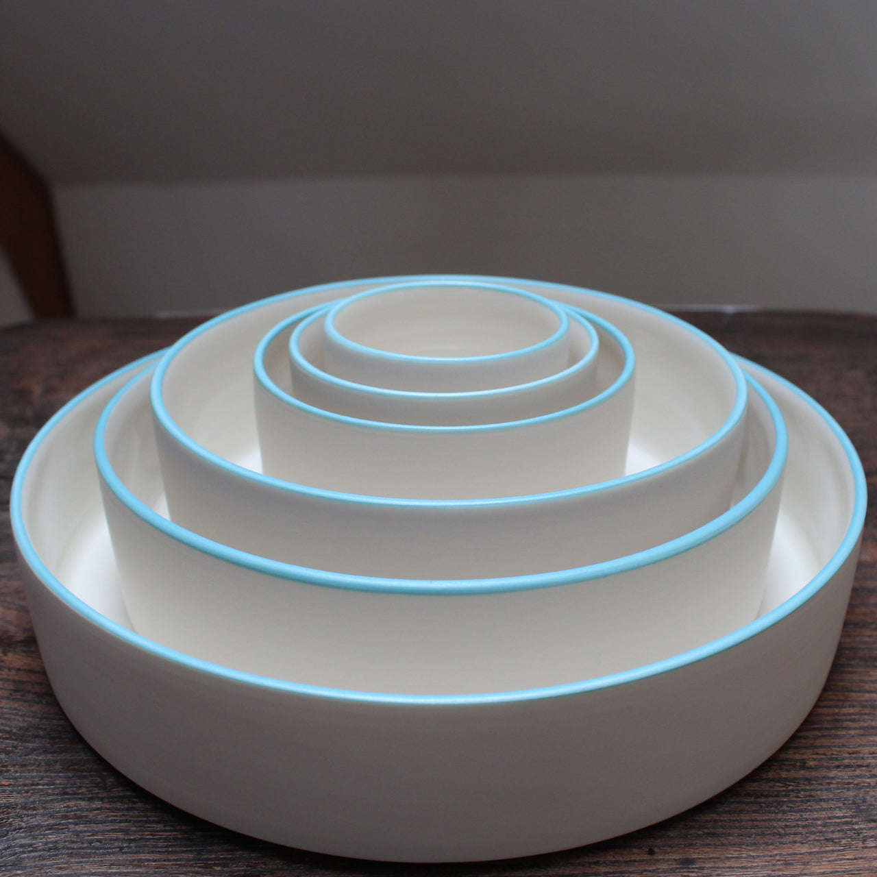 Six stacked white round bowls with a blue rim on a wooden table