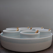 A set of even small bowls with turquoise stripes  and wooden spoons set inside a larger serving dish