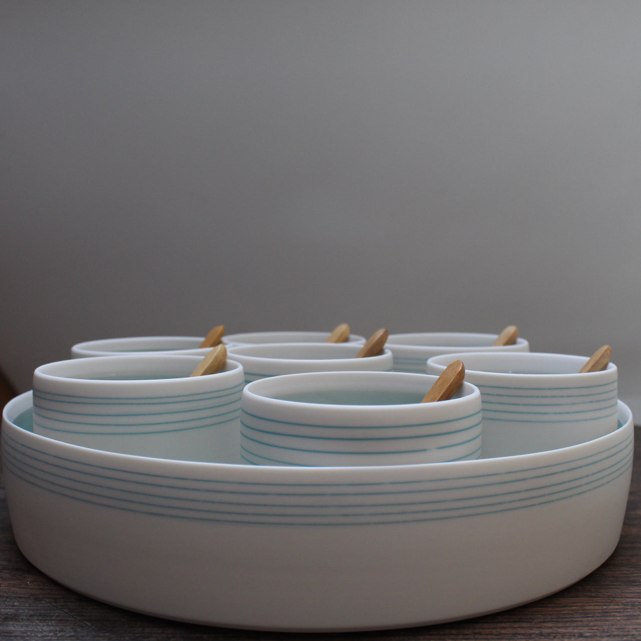 A set of even small bowls with turquoise stripes  and wooden spoons set inside a larger serving dish