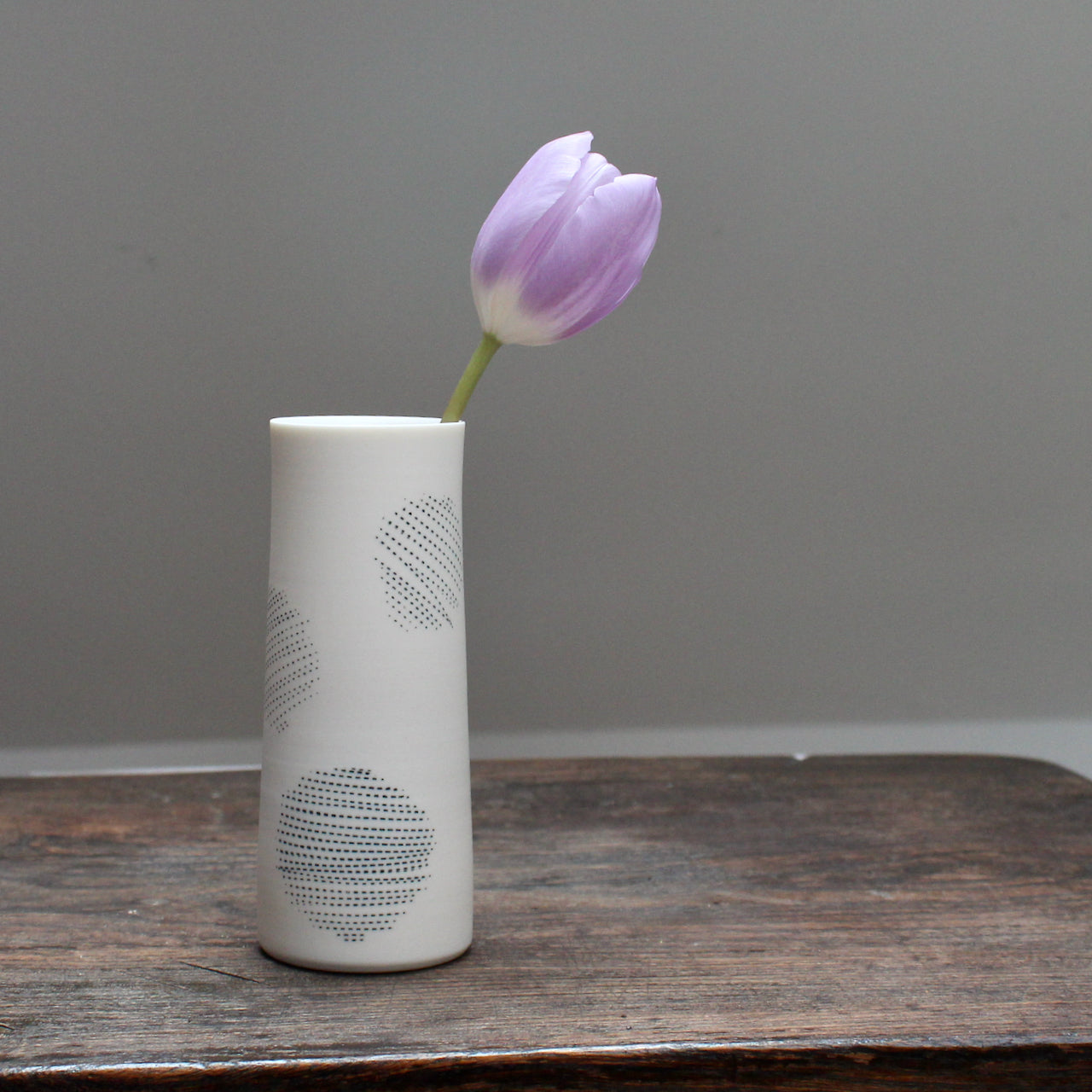narrow ceramic white stem vase decorated with abstract circles with a lilac tulip in it