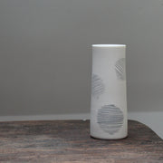 A narrow ceramic white stem vase decorated with abstract circles sitting on a wooden table