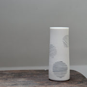 narrow ceramic white stem vase decorated with abstract circles sitting on a wooden table