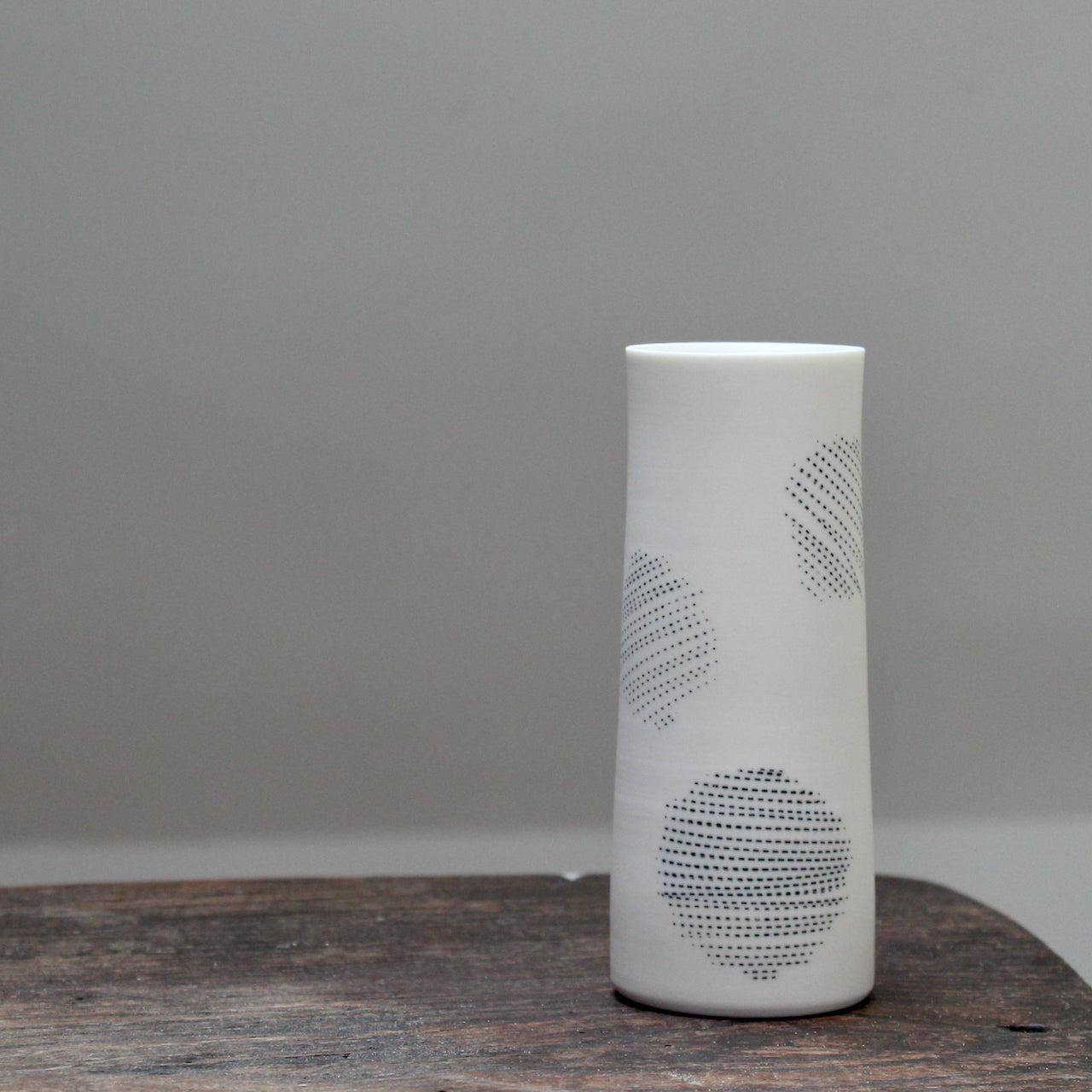 narrow ceramic white stem vase decorated with abstract circles sitting on a wooden table