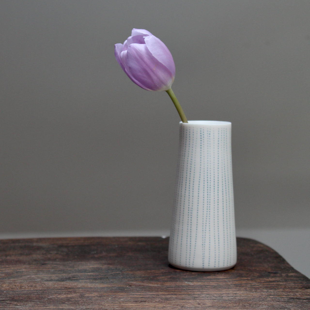 porcelain stem vase with blue vertical lines with lilac coloured tulip in it