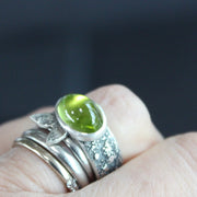 Carin Lindberg - Peridot ring in textured sterling silver with textured leaf detail shown being worn on a left hand with other dress rings.