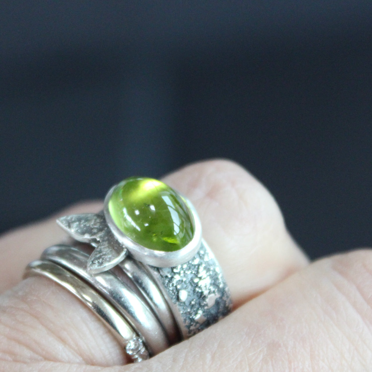 Carin Lindberg - Peridot ring in textured sterling silver with textured leaf detail shown being worn on a left hand with other dress rings.