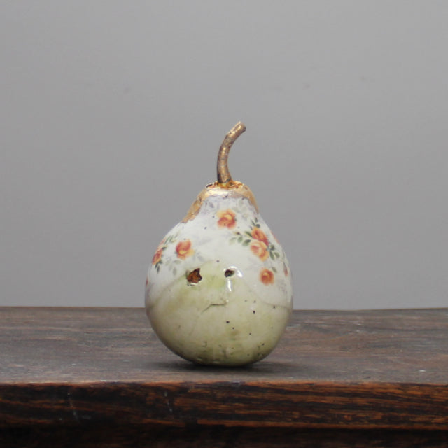 A large ceramic white pear with orange floral detail and a gold stalk by ceramic artist Remon Jephcott