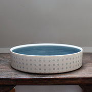 a porcelain serving dish decorated with with blue dots and a blue interior.