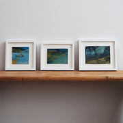 three small abstract landscape paintings by Alice Robinson-Carter in dark blues and yellows they are mounted and framed in white