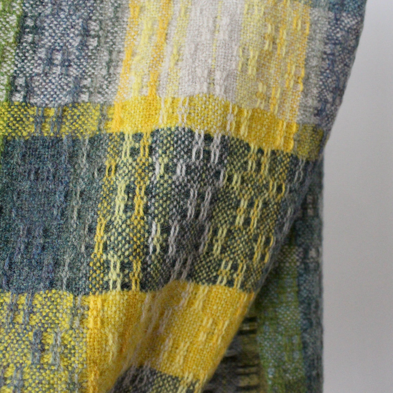 close up of textile designer Teresa Dunne's hand-woven scarf in shades of blue, green and yellow.