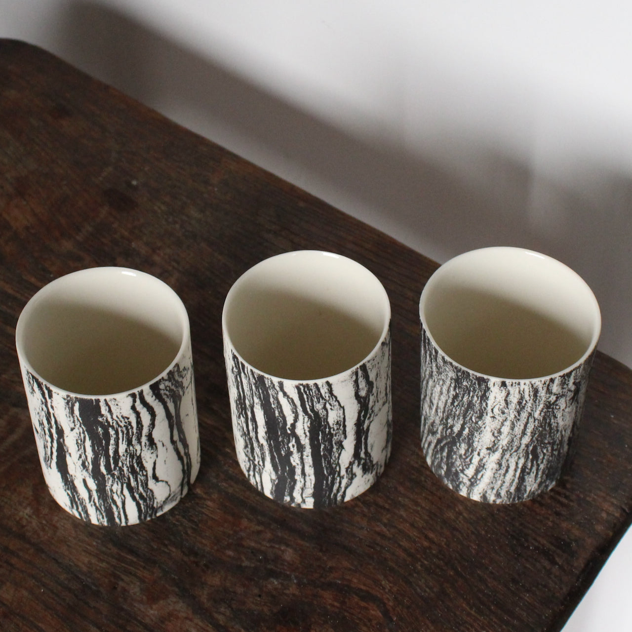 a  trio of small ceramic beakers by UK ceramicist Heidi Harrington with a black and white photo image of tree bark on the the exterior and cream glazed interior.