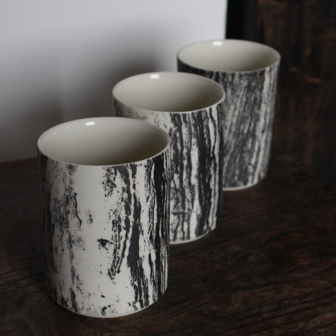 UK ceramicist Heidi Harrington trio of small ceramic beakers with a black and white photo image of tree bark on the the exterior and cream glazed interior