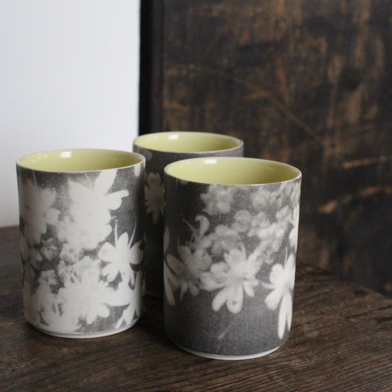 UK ceramicist Heidi Harrington trio of small ceramic beakers  with a black and white photo image of flower petals on the the exterior and pale yellow glazed interior 