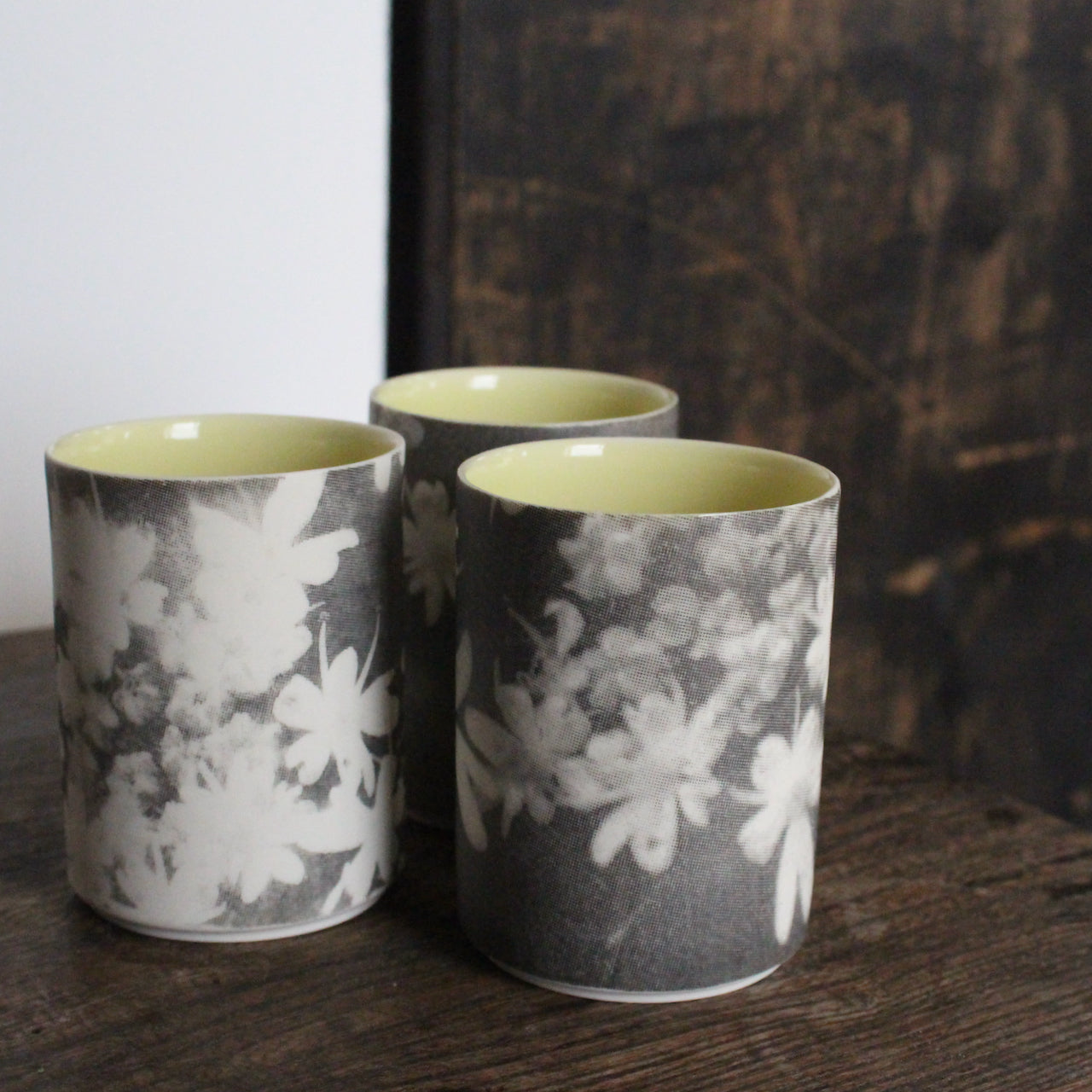 UK ceramicist Heidi Harrington trio of small ceramic beakers  with a black and white photo image of flower petals on the the exterior and pale yellow glazed interior