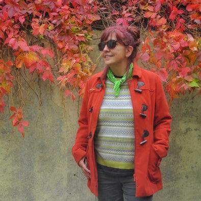 Cornish artist Siobhan Purdy wearing an orange coat and standing in front of a bush with orange and red leaves