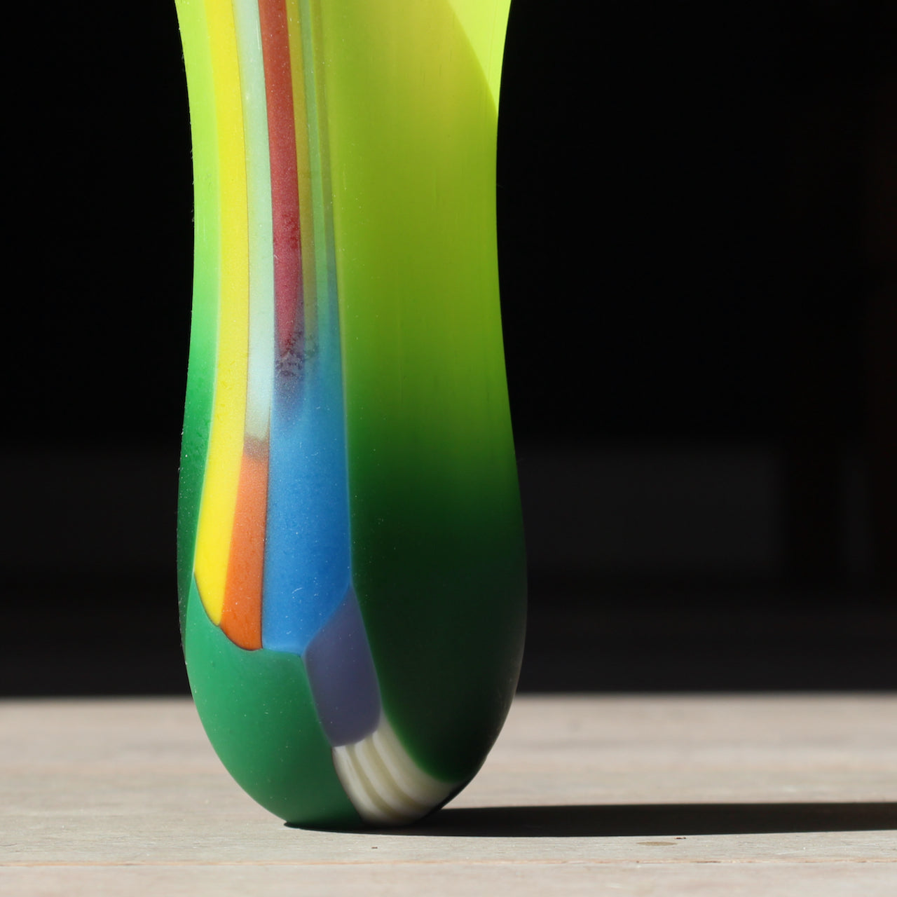 Narrow vibrant coloured glass vase in tones of green, yellow, blue and orange by glass artist Ruth Shelley.