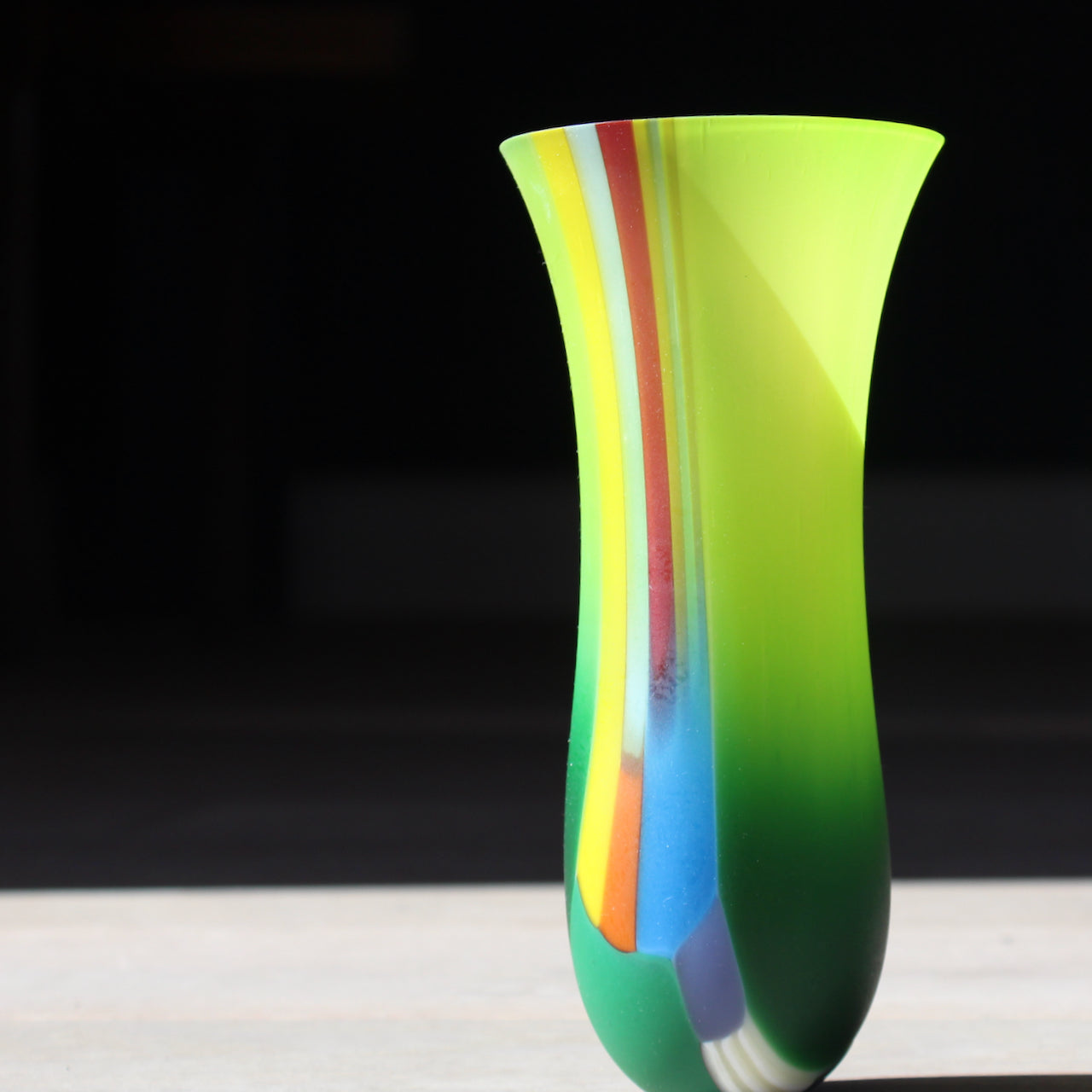 Narrow vibrant coloured glass vase by artist Ruth Shelley in tones of green, yellow, blue and orange